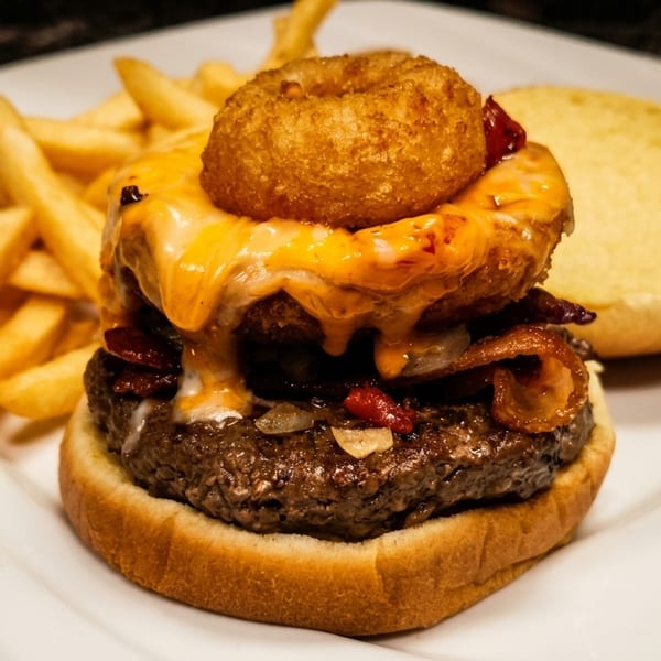 A loaded burger with melted cheese, bacon, onions, and onion rings, served with fries.