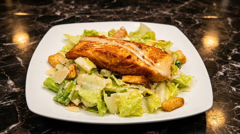Grilled salmon fillet on a bed of fresh Caesar salad with croutons and parmesan cheese.