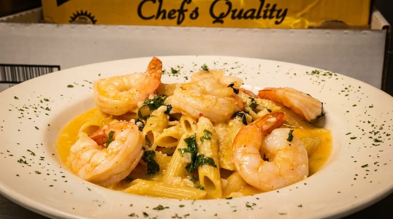 Penne pasta with shrimp, creamy sauce, and parsley in a white bowl.